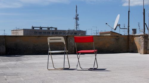Empty chairs against buildings in city against sky