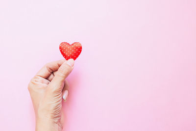 Close-up of hand holding heart shape over white background