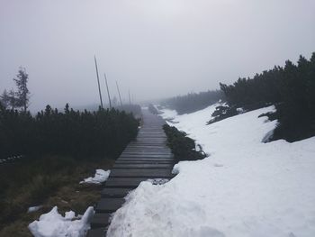 Narrow pathway along snow covered landscape against clear sky