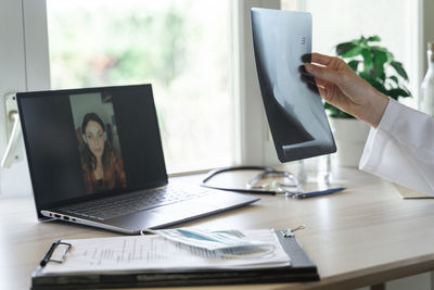 Young female doctor examining x-ray during online consultation from home office