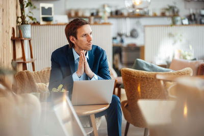 Freelancer with hands clasped sitting on chair at cafe