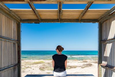 Rear view of friends standing in front of sea against clear blue sky