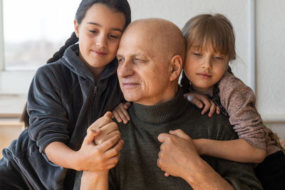 Grandfather and two granddaughters hugging on sofa at home