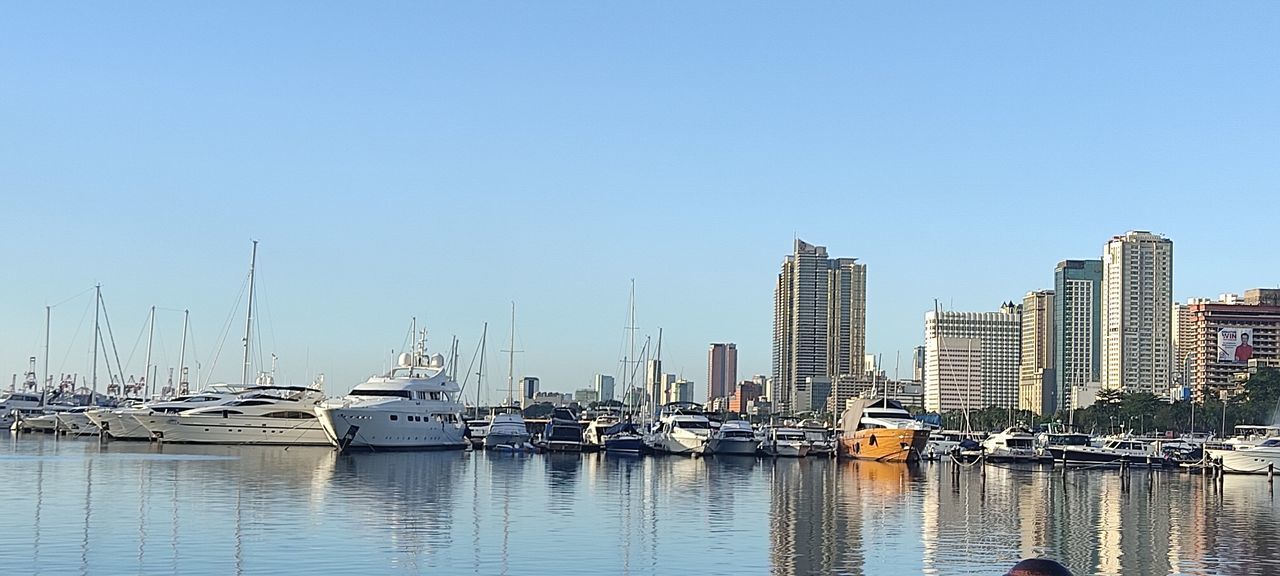 water, nautical vessel, sky, marina, transportation, harbor, dock, architecture, mode of transportation, city, cityscape, building exterior, ship, built structure, clear sky, skyline, sea, nature, building, sailboat, reflection, moored, boat, landscape, no people, travel destinations, bay, vehicle, port, urban skyline, blue, waterfront, day, travel, office building exterior, skyscraper, copy space, yacht, horizon, outdoors, watercraft, sunny, residential district, sunlight, sailing, pier