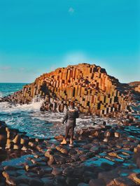 Man standing on rock by sea against clear blue sky