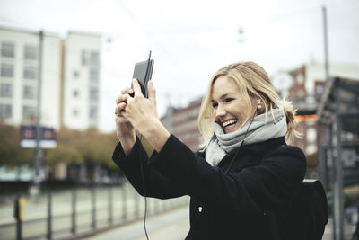 Smiling mid adult businesswoman talking selfie through mobile phone at tram station