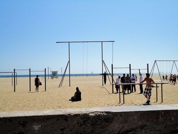 People playing soccer on beach against clear sky