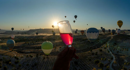 A hand cheers holding a champagne glass with alcohol against hot air balloon flight in cappadocia