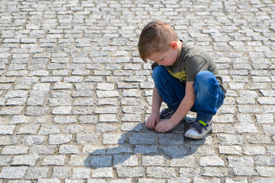 Boy sitting on the cracked earth and shows tongue.