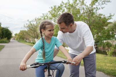 Father assisting daughter while riding bicycle on road