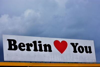 Close-up of text on road sign against sky