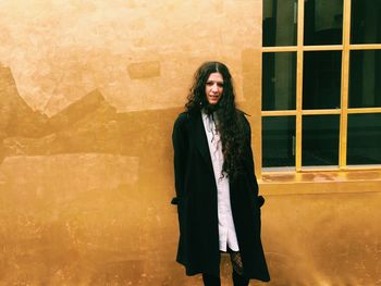 Portrait of young woman standing against wall