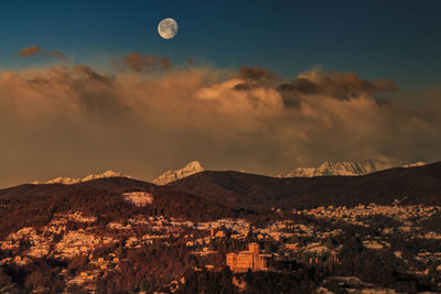 Townscape by mountains against cloudy sky during sunrise