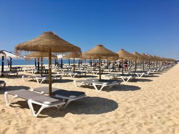 Lounge chairs and parasols on beach against clear blue sky