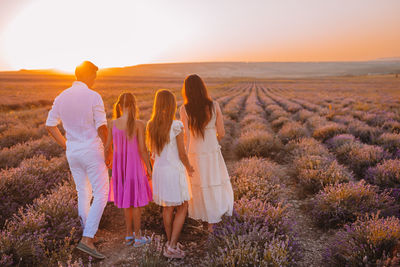 Rear view of women standing on landscape during sunset