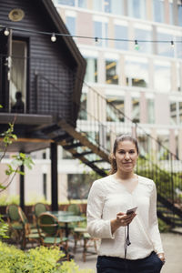 Portrait of confident businesswoman holding smart phone while standing at office yard