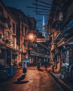 Rear view of people on illuminated street amidst buildings at night