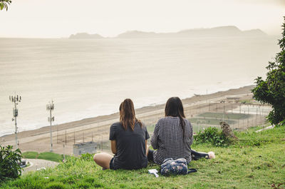 Rear view of woman sitting on shore against sky