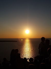 Silhouette people by sea against sky during sunset