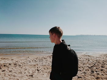 Teenage girl standing on beach against clear sky