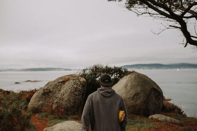 Rear view of man standing on rock by sea against sky