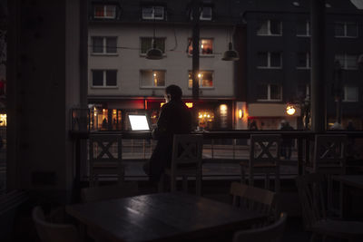 Businessman working on laptop sitting in front of glass window in cafe at night