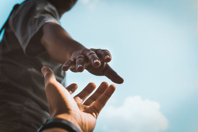 Cropped image of man reaching towards girlfriend hand against sky