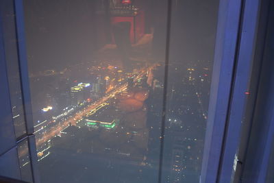 High angle view of illuminated street seen through glass window at night
