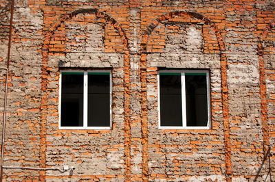 Unplastered brick wall of a building with two windows.