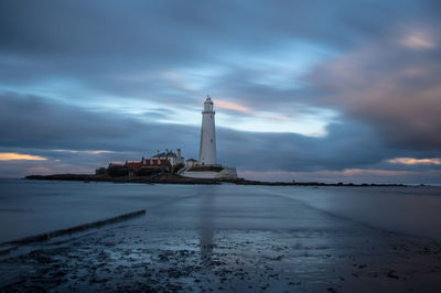 Lighthouse by sea against sky at dusk