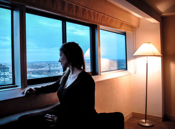 Woman looking through window while sitting on sofa at home