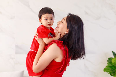 Smiling mother embracing son against wall at home