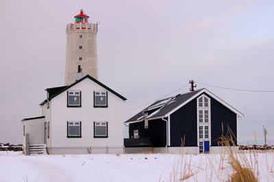 Lighthouse by building against sky during winter