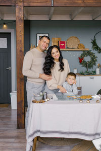 A stylish happy family is sitting at the table at the prepared gingerbread house for christmas
