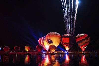 Illuminated hot air balloon over river against sky at night