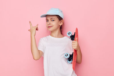 Portrait of young woman holding stethoscope against pink background