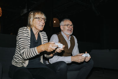 Senior woman playing video game sitting by male friend in gaming lounge