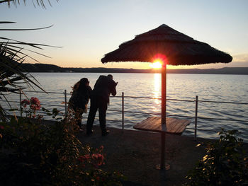 Silhouette people standing by sea against clear sky during sunset