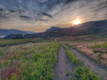 Road amidst field against sky during sunset