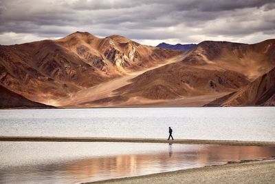 Distant view of silhouette man walking on footpath in lake against mountains