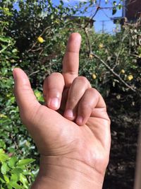 Close-up of hand showing middle finger against plants