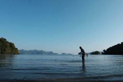 Man standing in sea against clear blue sky