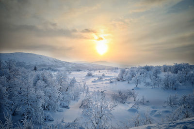 Snow covered landscape against sky during sunset