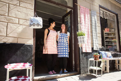 Low angle view of happy female owners standing at entrance of fabric shop