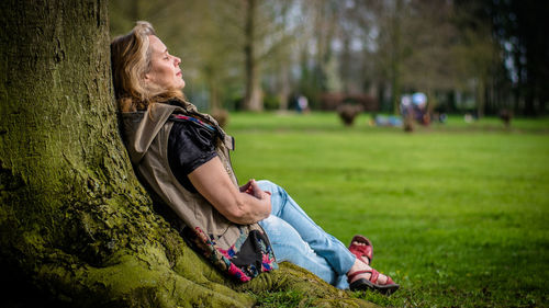 Woman sitting by tree trunk at park