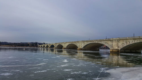 Arch bridge over river against sky during winter