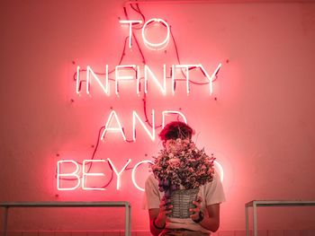 Man holding flower pot against illuminated text on wall