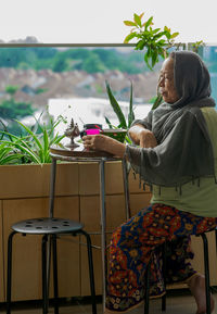 Senior malaysian muslim woman stay at home. sitting at the balcony apartment while having breakfast.