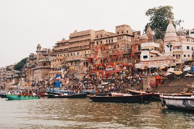 Boats moored in river by buildings against sky