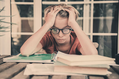 Frustrated boy siting next to books on desk at home